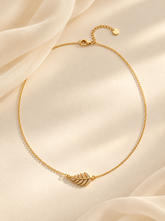 Collier Olivia doré à pendentif feuille, posé sur fond beige