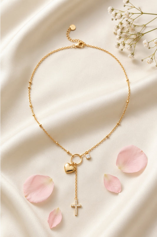 Collier Sofia doré avec cœur et croix scintillante posé sur fond beige